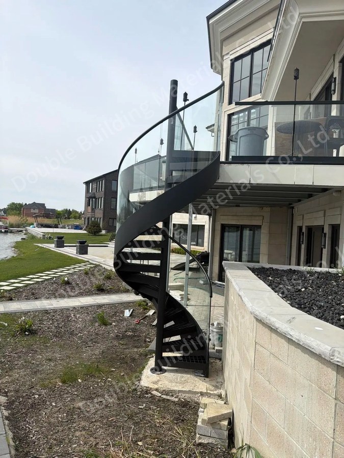 Outdoor black metal spiral staircase with grating treads and curved glass beside a Michigan house