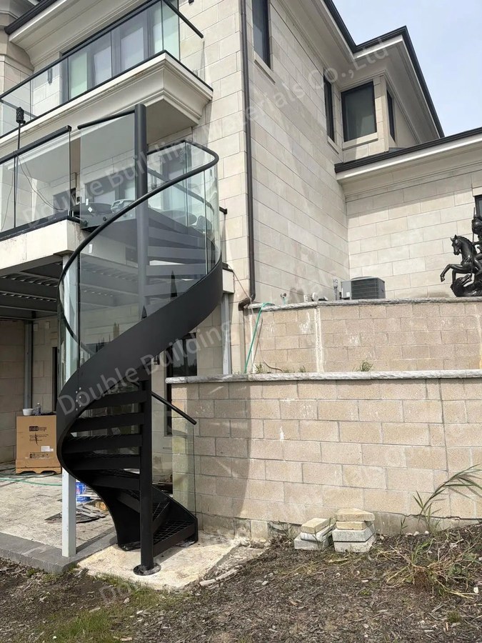 Side view of outdoor black metal spiral staircase with curved glass against stone facade