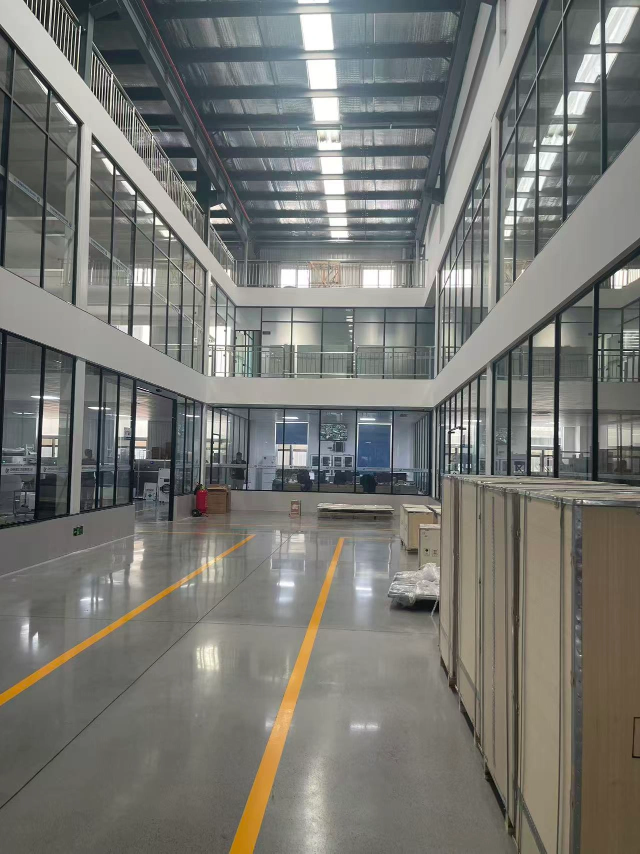 A spacious interior view of the final assembly workshop on the ground floor of the Geliss freeze-dryer factory, showcasing a modern, high-ceilinged layout with clean floors and yellow safety markings for production operations.
