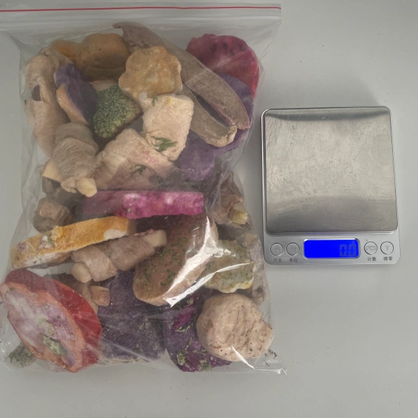 A high-volume bag of freeze-dried dog and cat treats next to a tared digital scale, illustrating how moisture elimination removes the need for expensive cold-chain logistics.